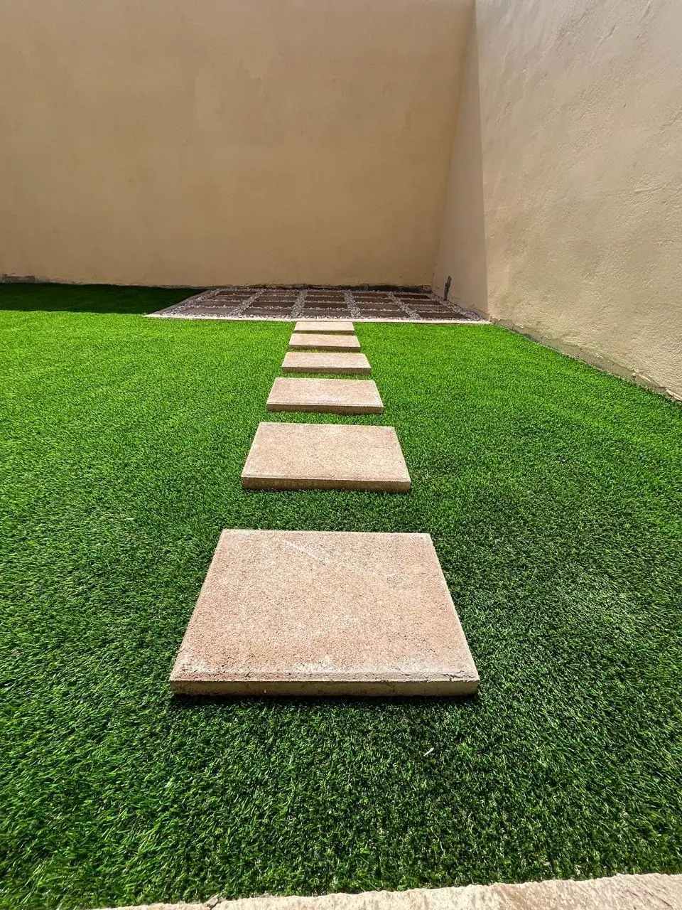 Sendero de huellas de concreto con césped artificial instalado por Jardines BR